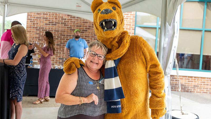 Lisa smiles for a picture with the Nittany Lion at an outdoor event.