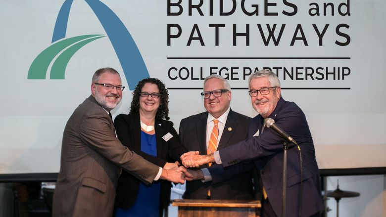 Four college presidents shake hands on stage.