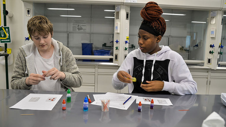 Two students sit at lab table and look at vials of faux blood.