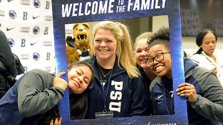 Three female students pose for a photo while holding a Penn State Welcome picture frame around themselves.