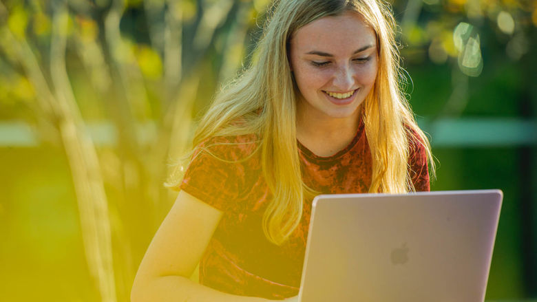 A blonde student works on  her laptop outdoors.