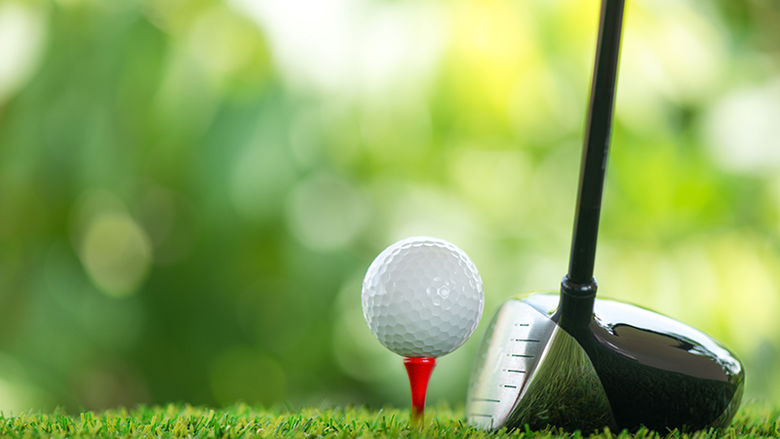 A close up picture of a golf ball sitting on a tee with a club behind it.