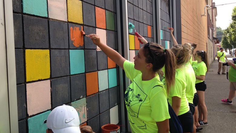 Members of the volleyball and softball teams paint bricks on a building in Aliquippa.