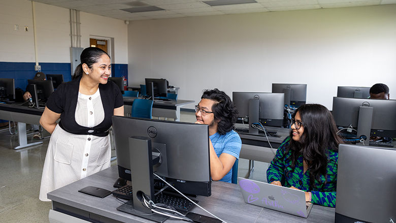 The professor stands to the left of the photo talking to two students who are seated to the right.Dr. Madhurima Ray, left, assistant professor of computer science at Penn State Beaver, interacts with Quang Nguyen, center, and Astha Kole, during class. Quang and Astha are both second-year computer science majors.  