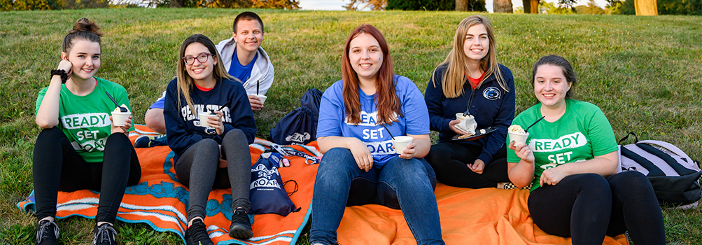 Six students dressed in shirts that say ready, set, roar sit on the ground with ice cream.
