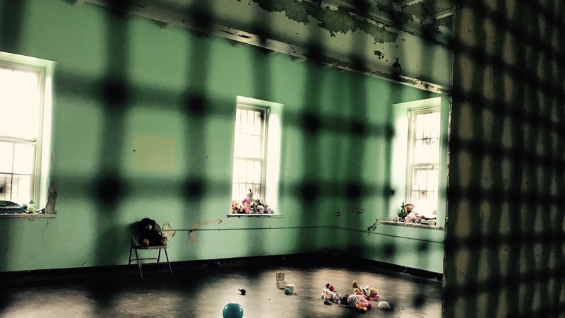 View, through caged door, of a nearly empty room in a former mental hospital.