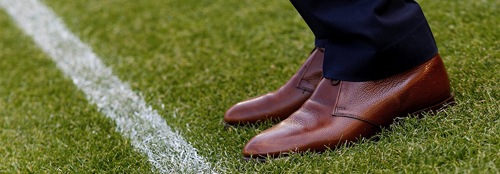 A person in dress shoes stands on a football field.