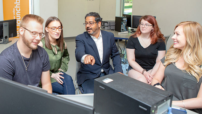 Ashu Kumar works with four students at a computer station.
