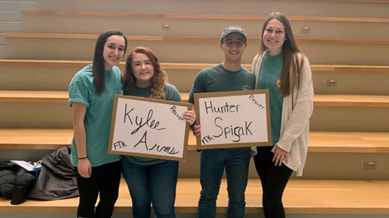 Penn State Beaver THON dancers Four people are pictured, three women and one man. They are holding signs displaying the THON dancer names.