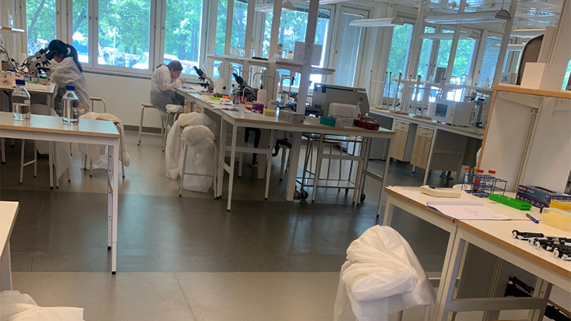 The photo shows a biology lab with labs, equipment and in the background large windows.
