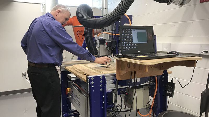 The professor looks over a wood carving the tool, which is mounted on a table in the maker space, is creating.