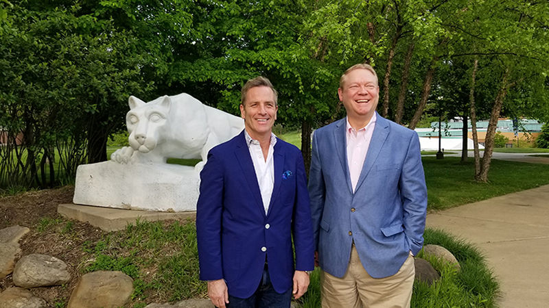 Two men wearing blazers stand in front of the Nittany Lion Shrine at Penn State Beaver.