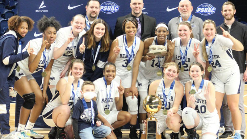 The women's basketball team and coaches are pictured as a group with the championship golden basketball trophy.
