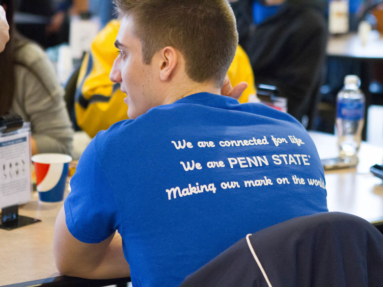 A student at a community service event wears a shirt that says we are connected for life; we are penn state, making our mark on the world.
