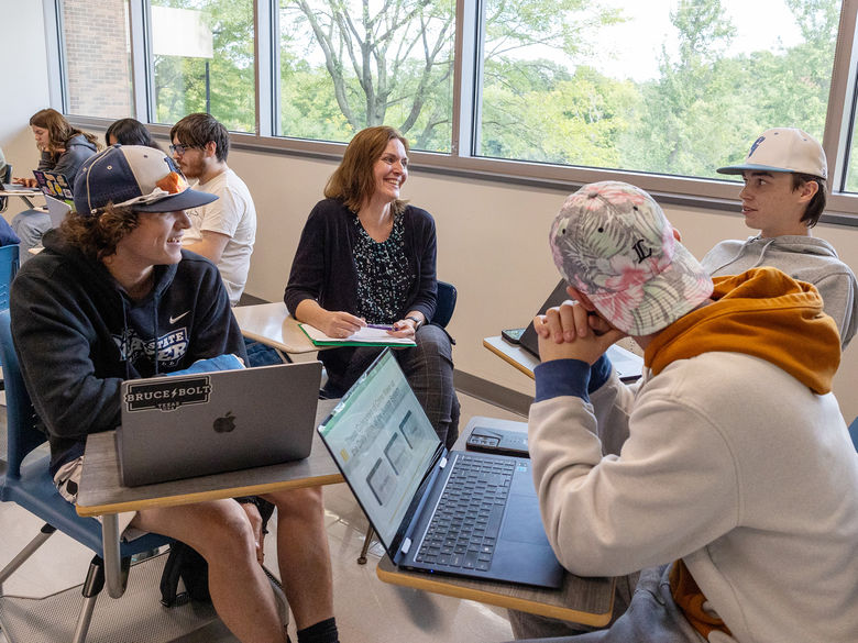 Professor Mari Pierce sits with a group of students in her classroom.