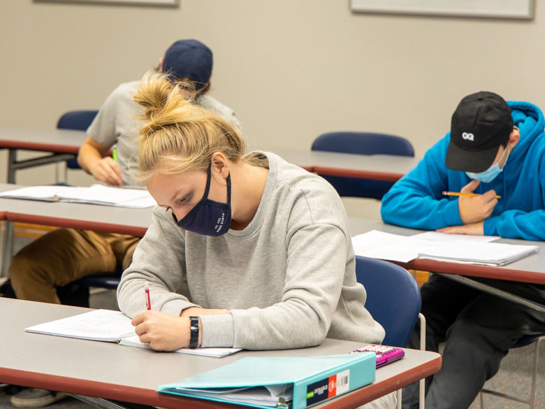 three students wearing masks work on a test