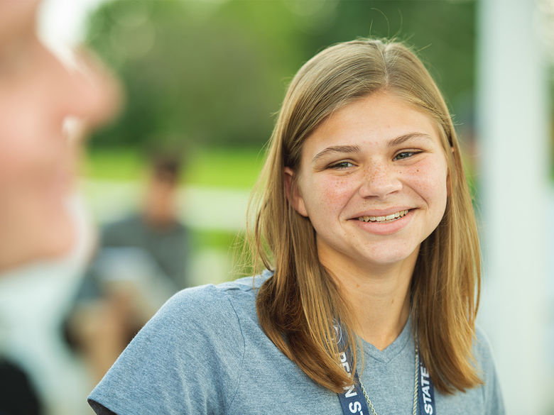 A female student wearing a Penn State lanyard smiles at another student.
