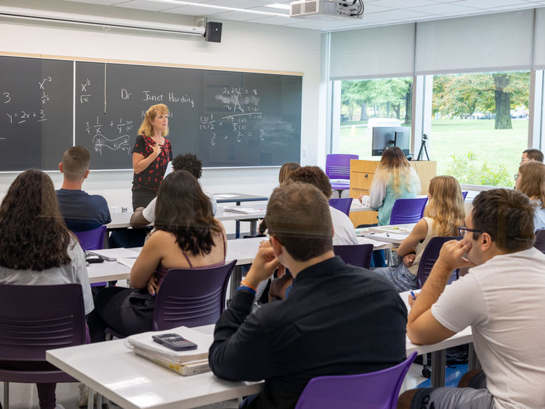 a math professor stands at the front of a classroom full of students