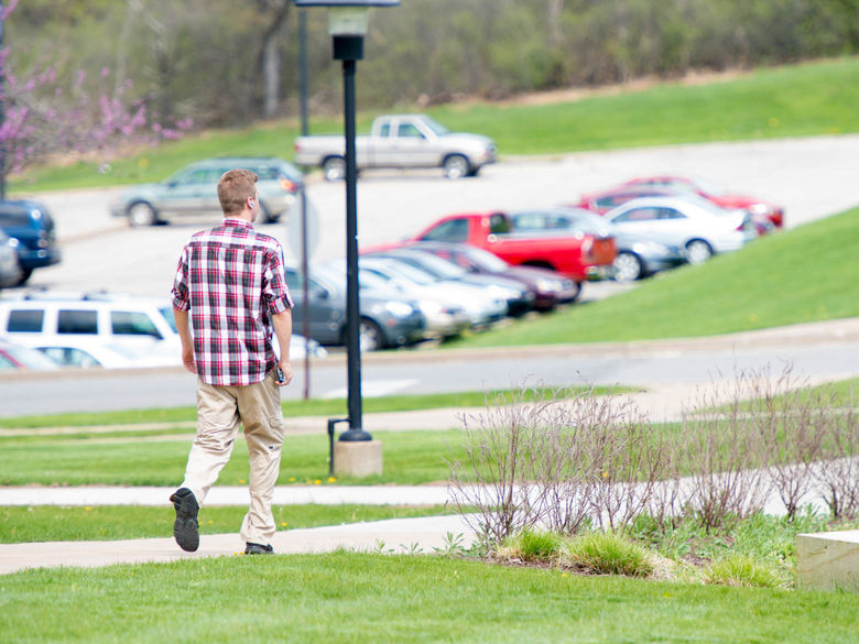 A male student walks past cars in one of the parking lots.