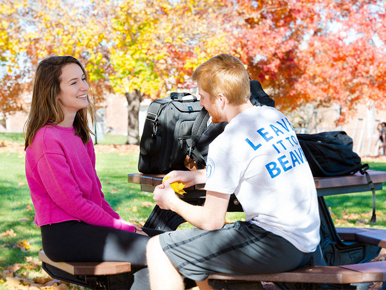 A female student and a male student sit and talk at a picnic table on campus.