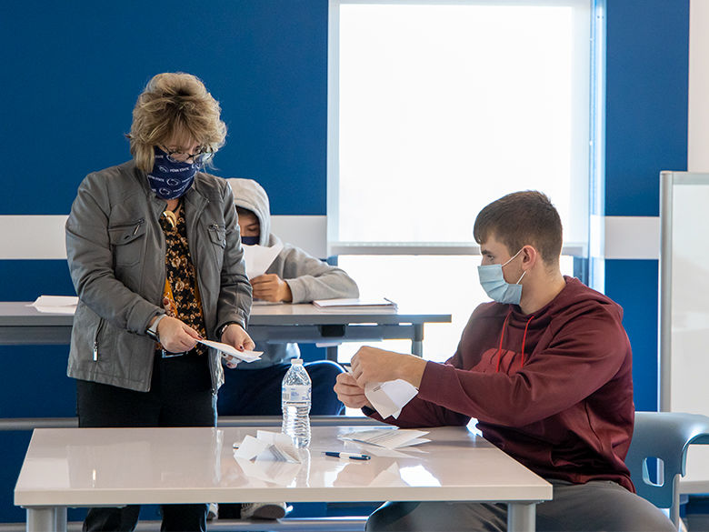 Professor Tiffany MacQuarrie consults with a student on the proper way to fold a paper airplane. Both are wearing masks.