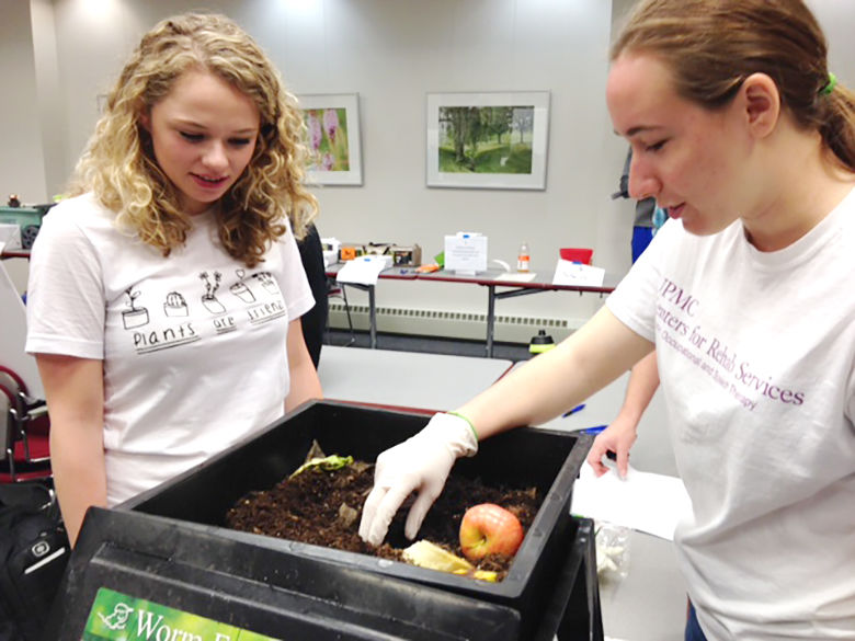 A student shows her composting project to another student.