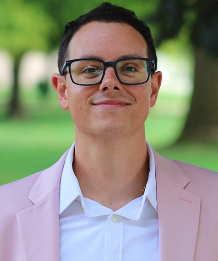 A man wearing glasses and a pink jacket standing outdoors