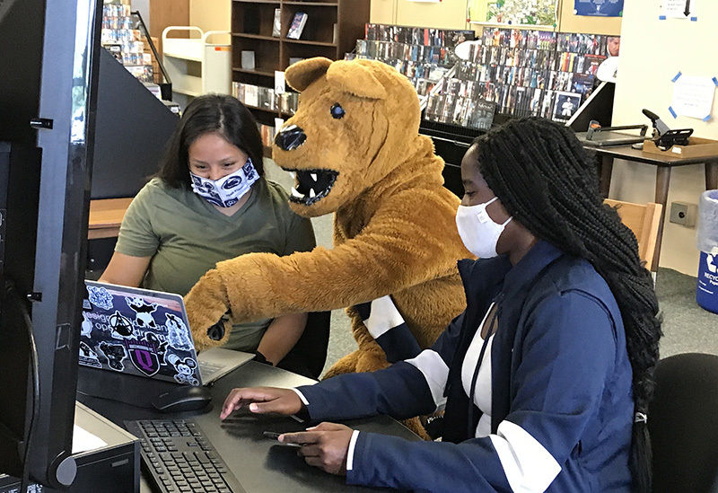 The Nittany Lion looks at a computer program with two female students in the campus library