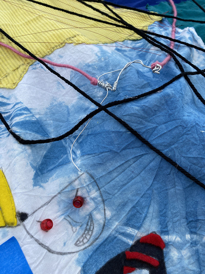 A close up view of a flag with various textiles that shows string representing thoughts coming from someone's head.