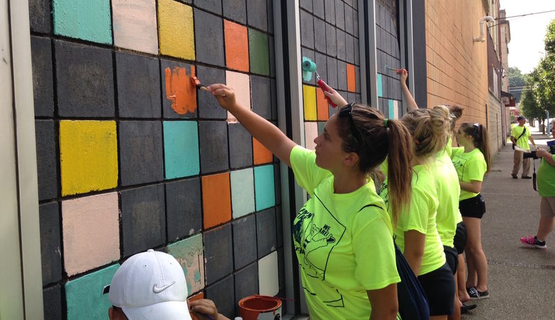 Members of the volleyball and softball teams paint bricks on a building in Aliquippa.