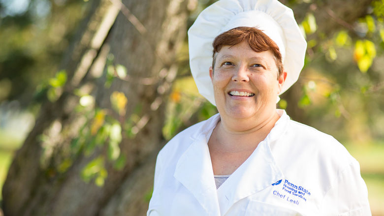 Lesli Kelly, wearing her chef's uniform, poses in front of a tree.