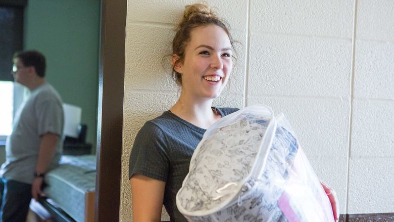 Student Allyson Pinto holds a sleeping bag in her arms while standing in Harmony Hall.