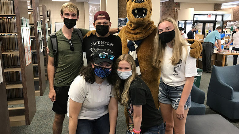 The Nittany Lion poses for a photo with a group of students near the stacks in the Penn State Beaver Library.