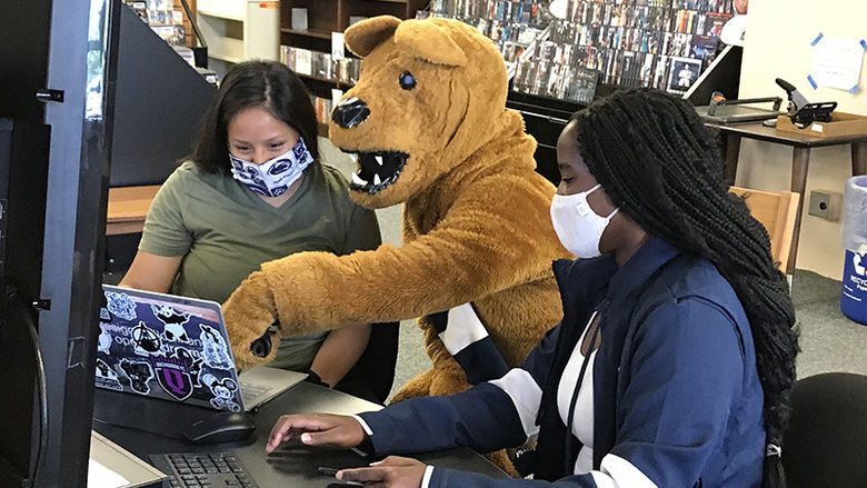 The Nittany Lion sits at a computer in the library with two female students.