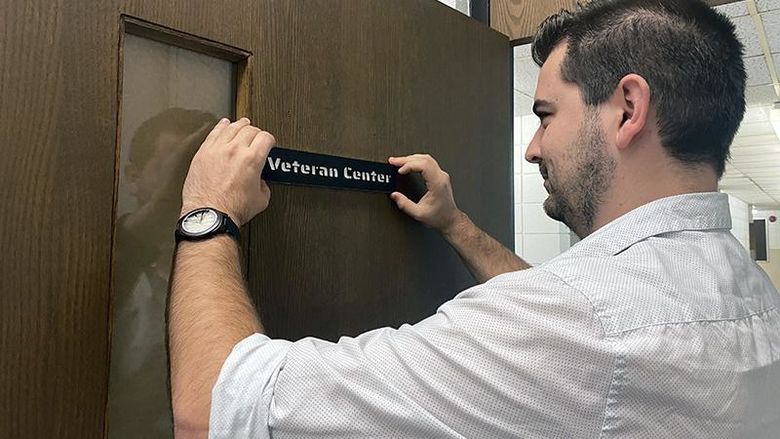 Student Josh Graham hangs a sign on the door of the new veterans lounge on campus