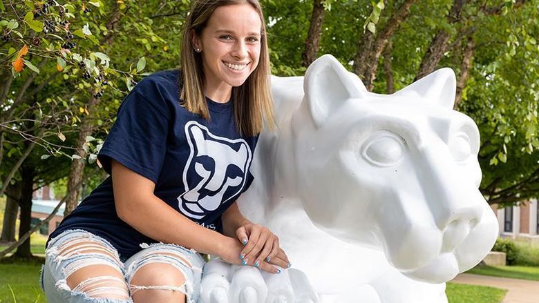 Alexis sits at the Lion Shrine on the Beaver campus wearing a navy and white Lion Ambassadors t-shirt.