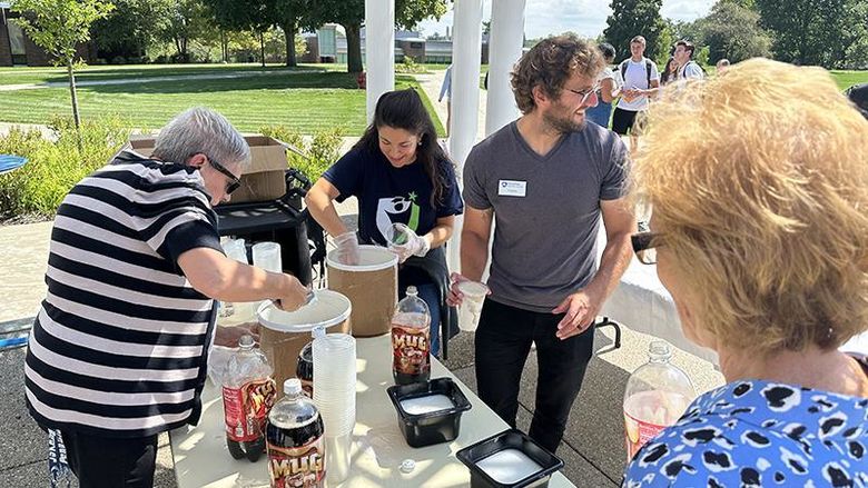 Four members of the committee stand outside on a sunny day making root beer floats.