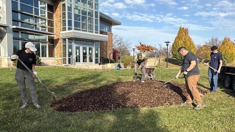 Four people work with shovels and rakes to prepare an area of mulch.