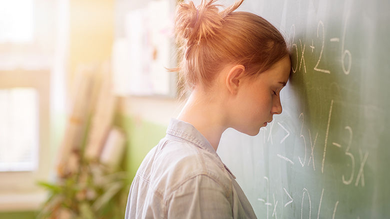 A student rests her forehead against a blackboard of math equations.