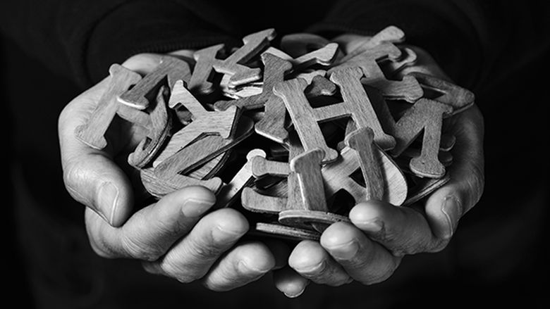 A black and white photos shows cupped hands holding wooden letters