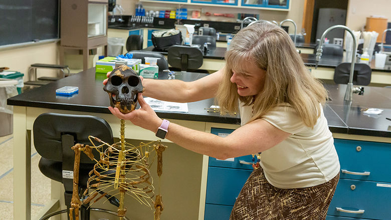 The professor stands to the right of a small skeleton as she assembles its head.