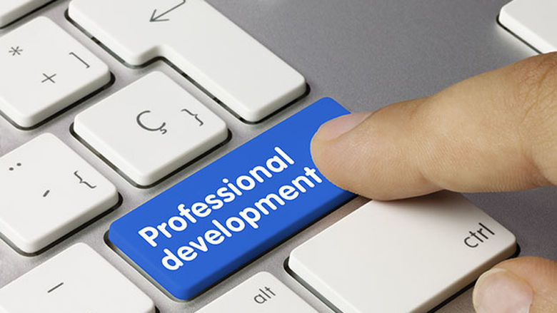 An index finger is about to push a button on a computer keyboard, but instead of a return key it is blue and says professional development.