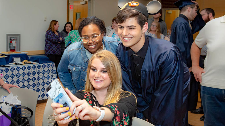 A graduate poses with two friends for a selfie.