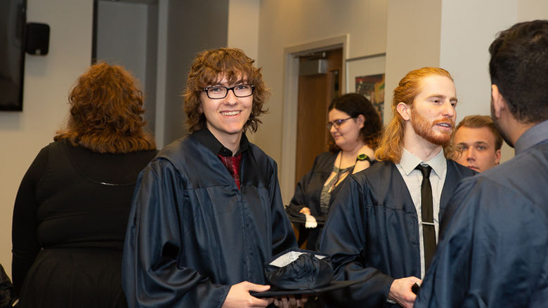 Penn State Beaver graduates wearing gowns talk after ceremony.