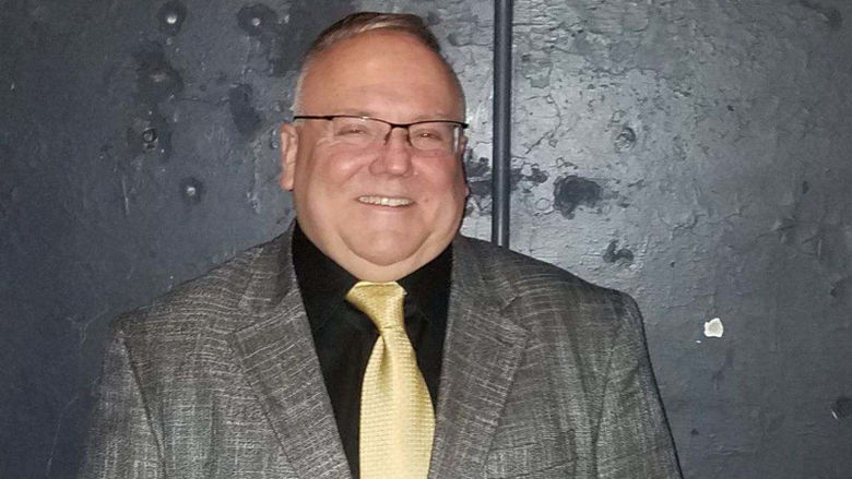 A photo of Scott Noxon wearing a grey jacket and yellow tie.