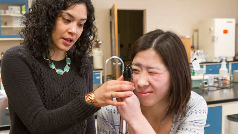Professor Stephanie Cabarcas-Petroski holds an ophthalmoscope up to a student's eye.