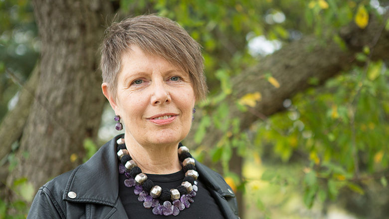 Robin Bower is pictured outdoors with trees in the back ground. She is wearing a black shirt, a chunky necklace and has short hair with side-swept bangs.