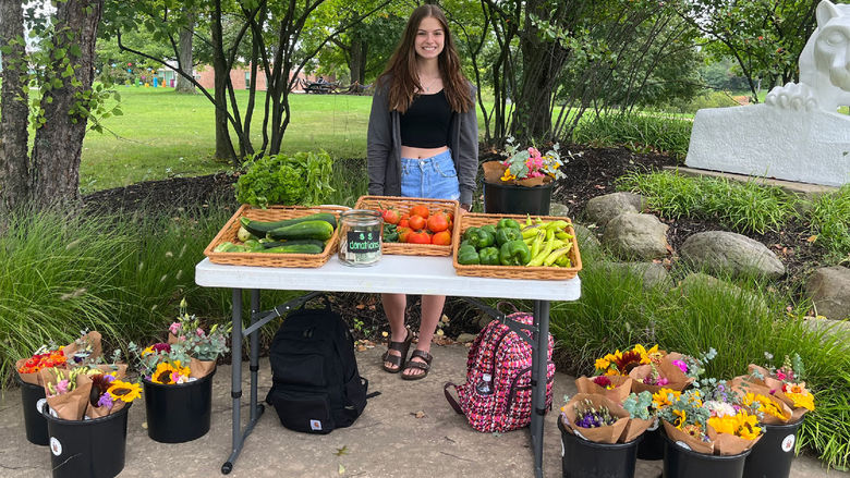 A female student stands behind a table loaded with fresh-cut flowers