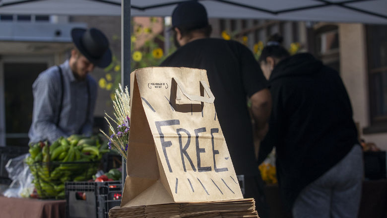 A paper bag labeled "Free Food" sits in front of a stall of fresh produce