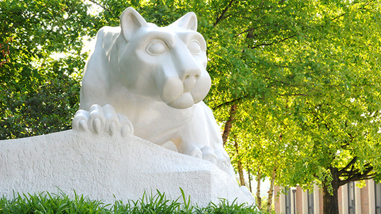 A photo of the Lion Shrine on campus with trees above it and sun shining through the green leaves